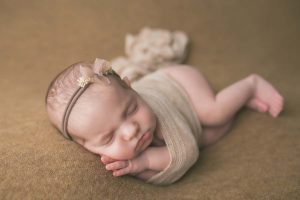 Newborn Girl portrait side sleeping on brown fabric with peach headband