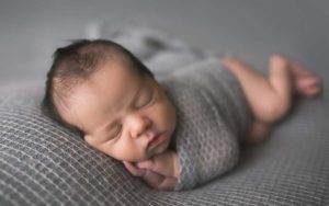 Newborn boy posed contently on grey fabric