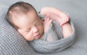 Newborn boy posed sleeping on grey fabric swaddled in grey